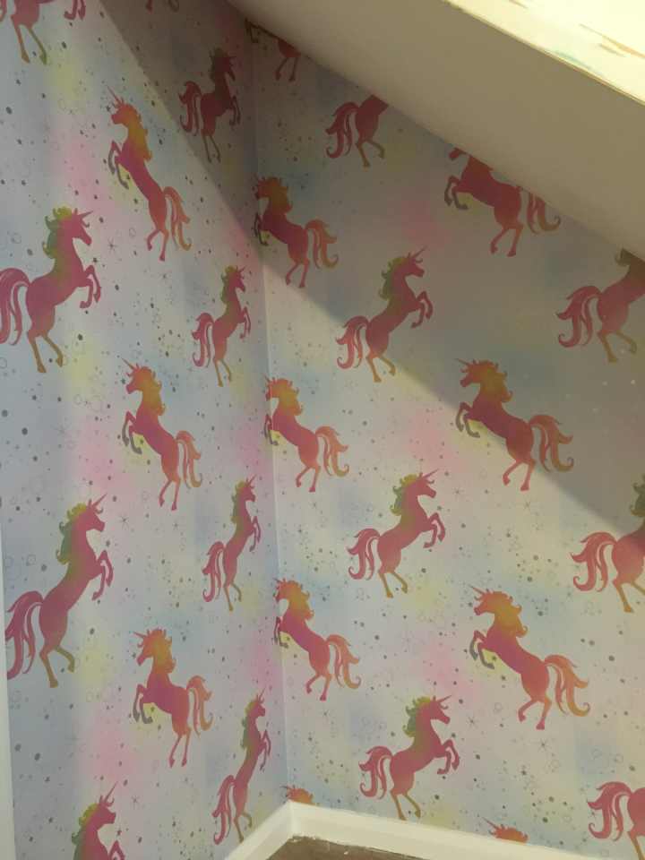 Under stairs wall wallpapered with shiny pink unicorns.