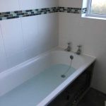 A half full bath with white tiles around on 2 sides.