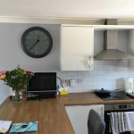 Kitchen area showing large round clock on grey wall.